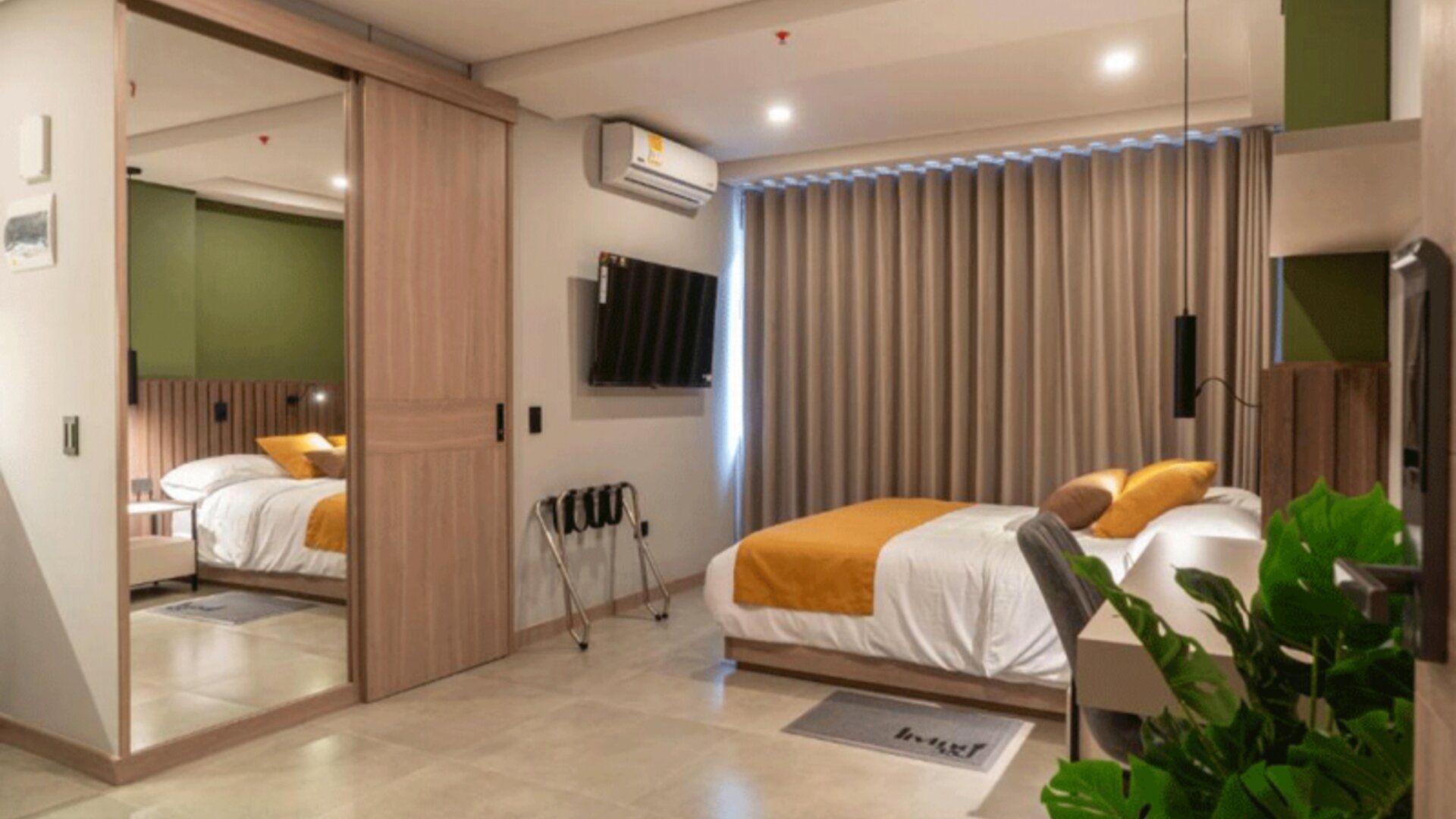 Modern guest room with a double bed, mustard accent cushions, mirrored wardrobe, wall-mounted television, and potted plant at Hotel Living 35 Suites.