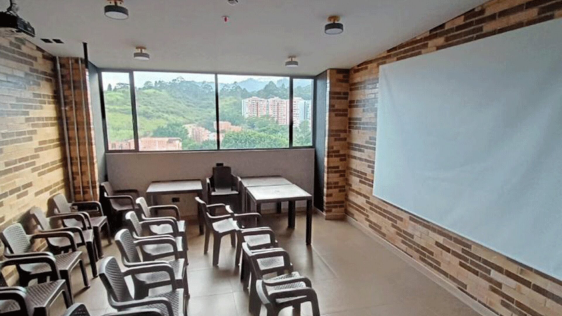 Meeting room with rows of chairs and tables, a large presentation board, exposed brick walls, and windows overlooking greenery at Hotel Living 35 Suites.