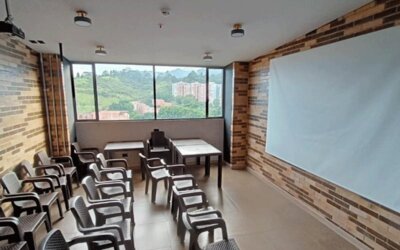 Meeting room with rows of chairs and tables, a large presentation board, exposed brick walls, and windows overlooking greenery at Hotel Living 35 Suites.