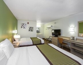 Guest room with two double beds, white bedding, green patterned runners, bedside lighting, a television, and a long desk with a mirror at American Inn Carlisle.