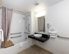 Accessible bathroom with a bathtub, shower curtain, grab bars, wall-mounted mirror, black countertop, and white vessel sink at American Inn Carlisle.