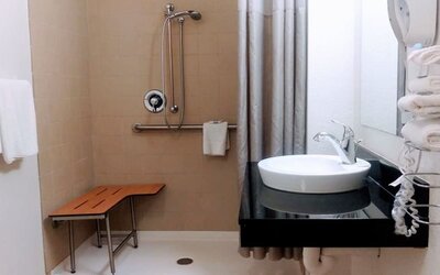 Bathroom with a walk-in shower, grab bars, shower seat, white vessel sink, black countertop, and folded towels at American Inn Carlisle.