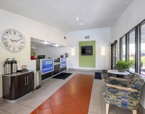 Reception and lobby area with tiled flooring, a front desk, a large wall clock, beverage station, seating, and windows at American Inn Carlisle.