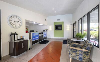 Reception and lobby area with tiled flooring, a front desk, a large wall clock, beverage station, seating, and windows at American Inn Carlisle.