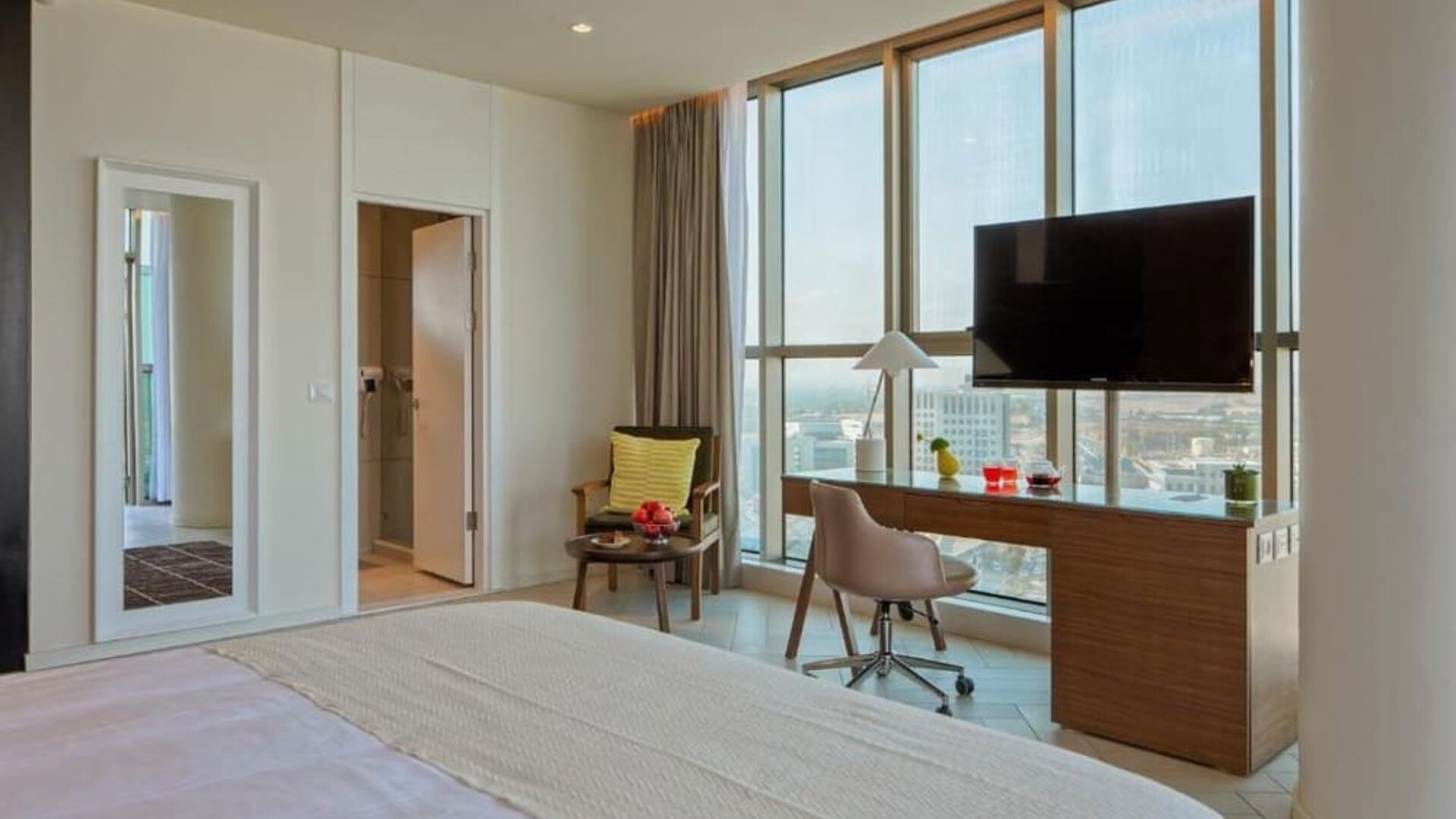Guest room with a king-size bed, white bedding, floor-to-ceiling windows, a desk and chair, television, and a separate seating area at Prima Millennium.