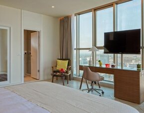 Guest room with a king-size bed, white bedding, floor-to-ceiling windows, a desk and chair, television, and a separate seating area at Prima Millennium.
