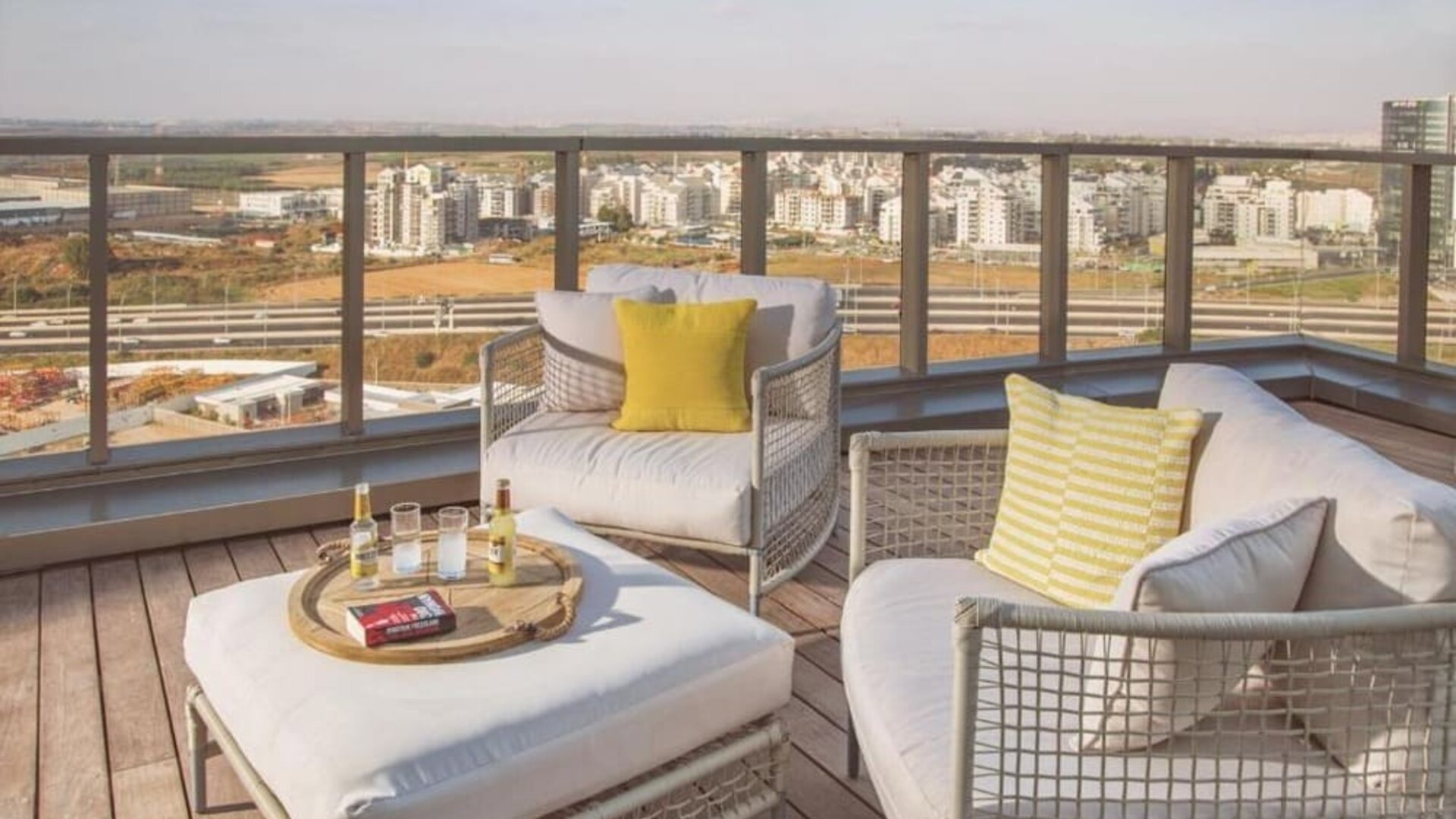 Rooftop lounge area with white cushioned outdoor sofas, yellow accent cushions, a low coffee table, and expansive city views at Prima Millennium.