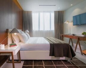 Bright guest bedroom with a king-size bed, white bedding, dark throw, wood-panelled wall, bedside table, television, and desk at Prima Millennium.