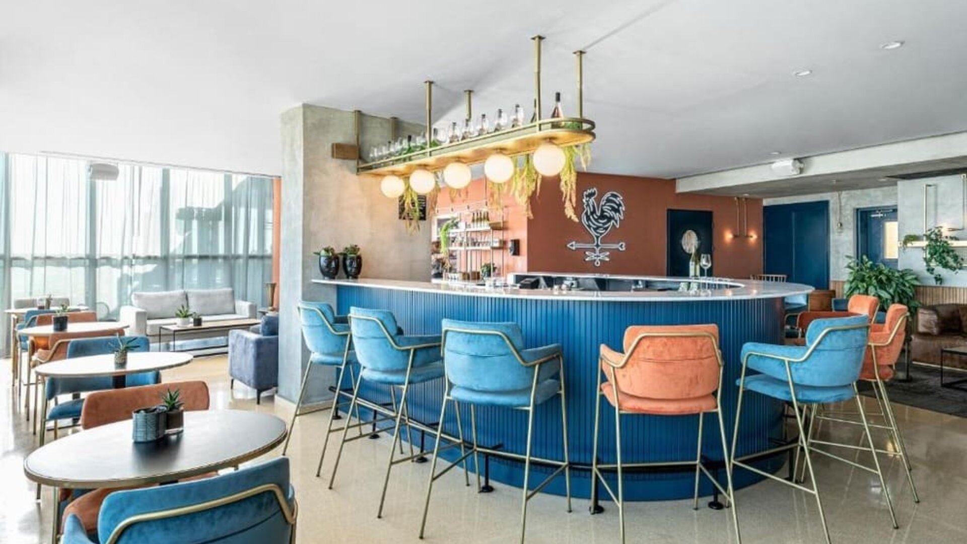 Modern hotel bar with a curved blue counter, colourful upholstered bar stools, pendant lighting, and lounge seating at Prima Millennium.