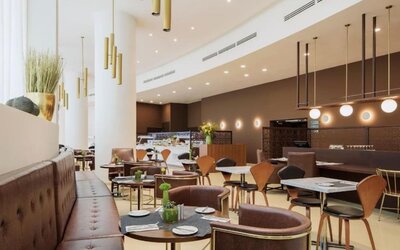 Hotel restaurant and dining area featuring brown upholstered seating, wooden chairs, round tables, decorative pendant lights, and a buffet counter at Prima Millennium.