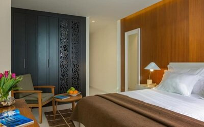 Guest room with a king-size bed, white bedding, a brown throw, wood-panelled accent wall, bedside lamps, wardrobe, and seating area at Prima Millennium.
