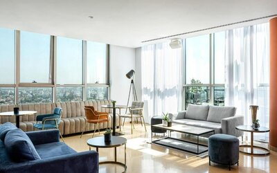 Spacious hotel suite lounge with floor-to-ceiling windows, city views, blue and neutral sofas, accent chairs, and contemporary coffee tables at Prima Millennium.