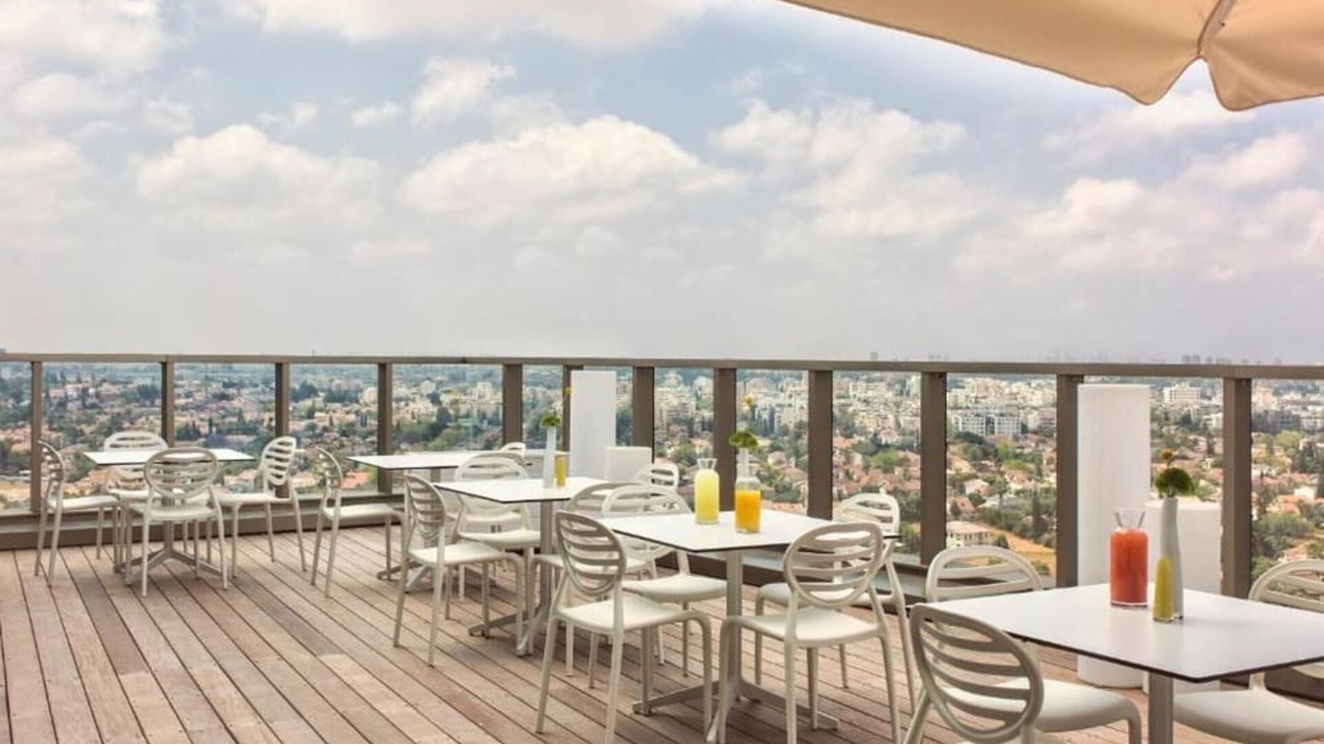 Rooftop dining terrace with wooden decking, white tables and chairs, parasols, and panoramic city views at Prima Millennium.