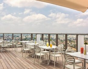 Rooftop dining terrace with wooden decking, white tables and chairs, parasols, and panoramic city views at Prima Millennium.