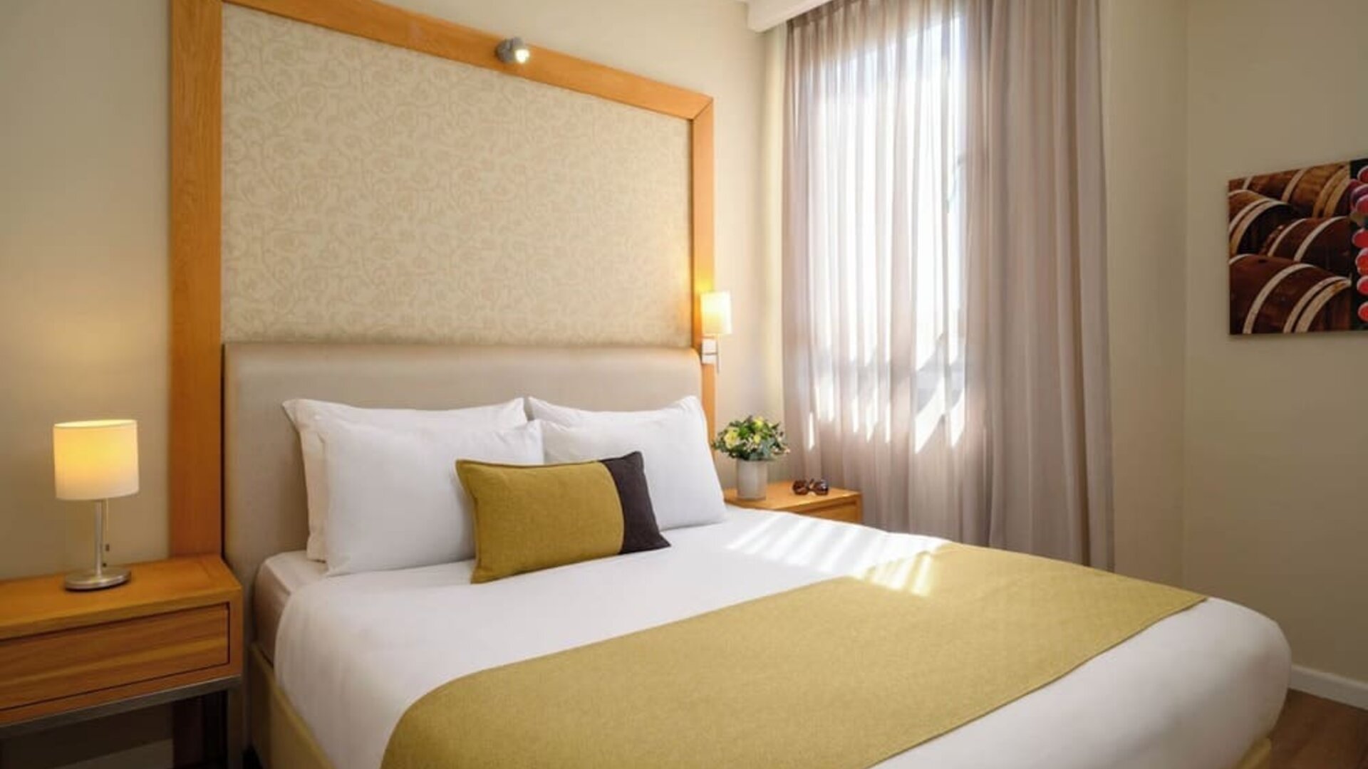 Guest room featuring a king-size bed with white bedding, a gold bed runner, decorative accent cushions, wooden bedside tables, and a large upholstered headboard at Prima Park Hotel.
