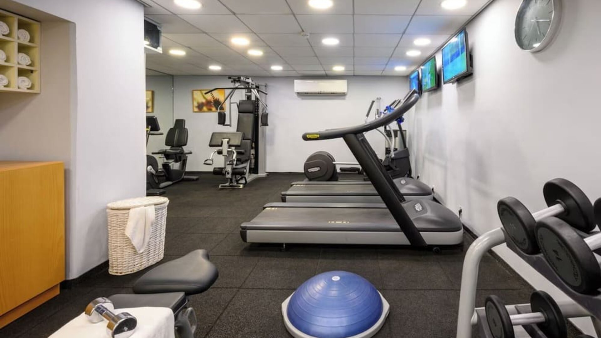 Hotel fitness centre equipped with treadmills, weight machines, dumbbells, an exercise ball, and wall-mounted televisions at Prima Park Hotel.