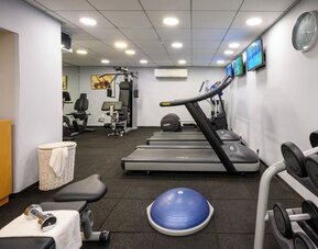 Hotel fitness centre equipped with treadmills, weight machines, dumbbells, an exercise ball, and wall-mounted televisions at Prima Park Hotel.