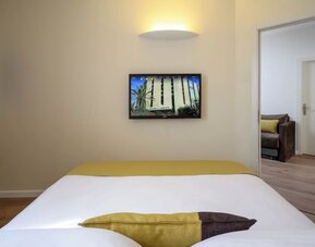 Close-up view of a neatly made king-size bed with white bedding, a gold bed runner, and contrasting decorative cushions at Prima Park Hotel.