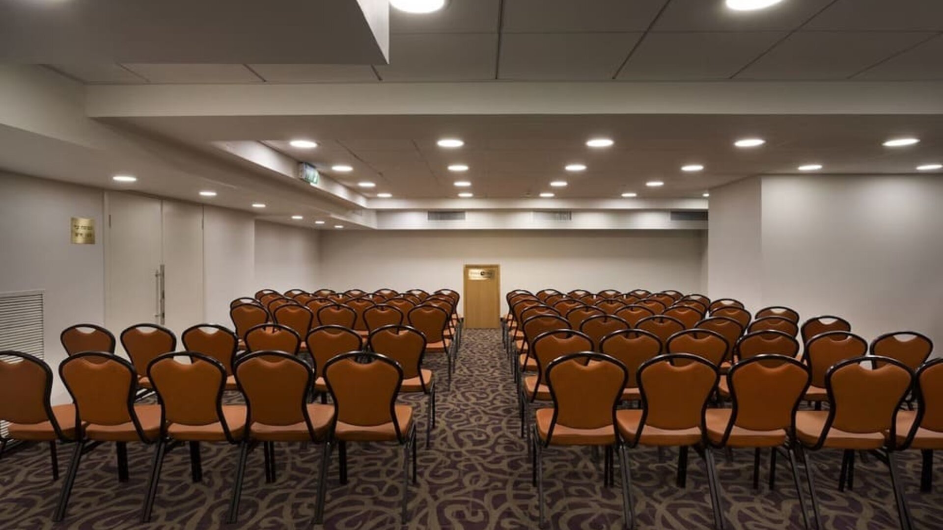 Meeting room arranged classroom-style with rows of chairs, patterned carpeting, a presentation area, and overhead lighting at Prima Park Hotel.