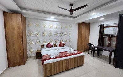 Guest bedroom with a wooden double bed, white bedding, red decorative cushions and bed runner, patterned feature wall, wardrobes, ceiling fan, and a small table with chairs beside the window at Hotel Urban Abode.