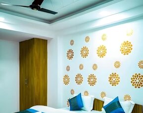 Guest room with a double bed, white bedding, teal and blue accent cushions, a matching bed runner, gold floral wall decorations, wooden wardrobe, and ceiling fan at Hotel Urban Abode.