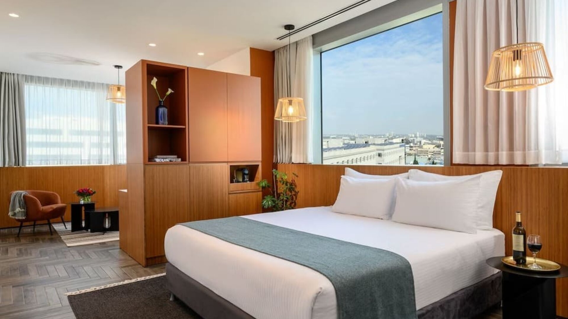 King bed with white bedding, teal runner, wood-panelled walls and city views at Prima Link.