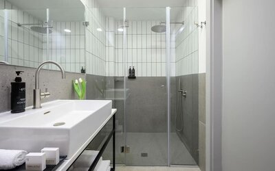 Walk-in shower with glass doors, rainfall showerhead, tiled walls and white vanity at Prima Link.