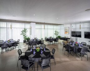 Meeting space with round tables, black tablecloths, chairs and floor-to-ceiling curtains at Prima Link.