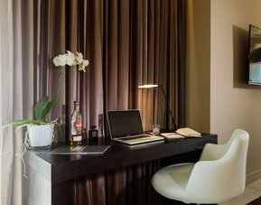 Work desk with an open laptop, notebook, white chair and potted orchid at Prima Link.