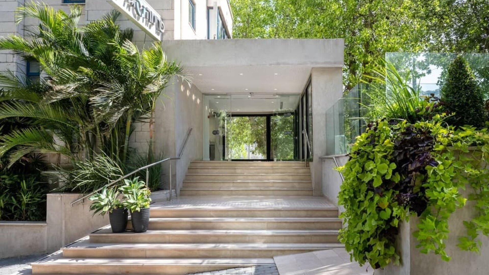 Hotel entrance with wide stone steps, glass doors and landscaped greenery at Prima Galil Tiberias.