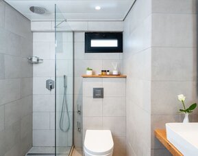 Modern bathroom with a glass-enclosed shower, rainfall showerhead and stone-effect tiles at Prima Galil Tiberias.