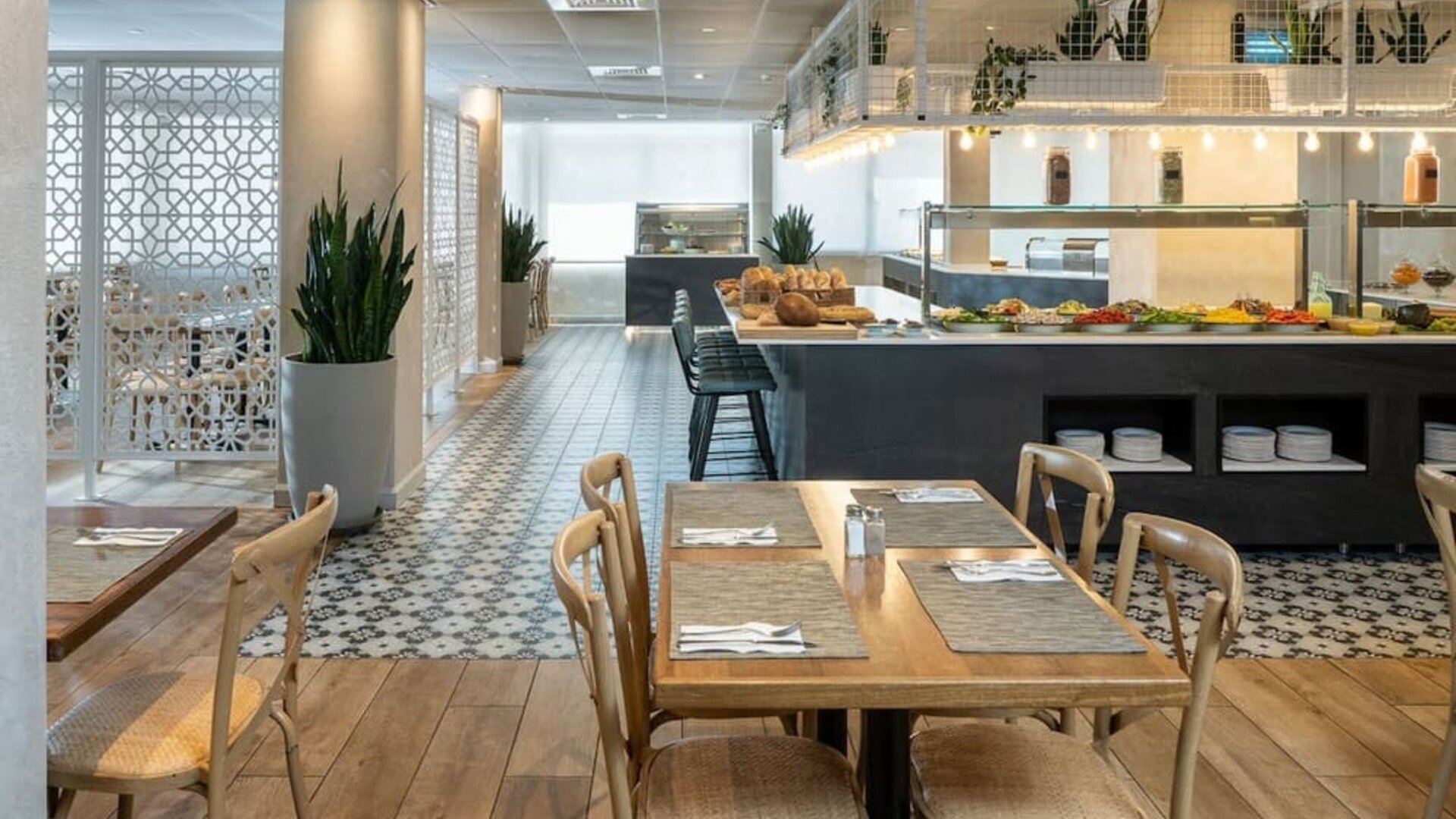 Restaurant dining area with wooden tables, patterned flooring and a buffet counter at Prima Galil Tiberias.