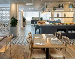 Restaurant dining area with wooden tables, patterned flooring and a buffet counter at Prima Galil Tiberias.
