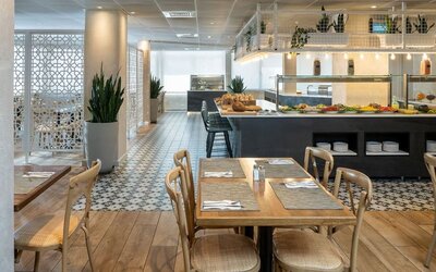 Restaurant dining area with wooden tables, patterned flooring and a buffet counter at Prima Galil Tiberias.
