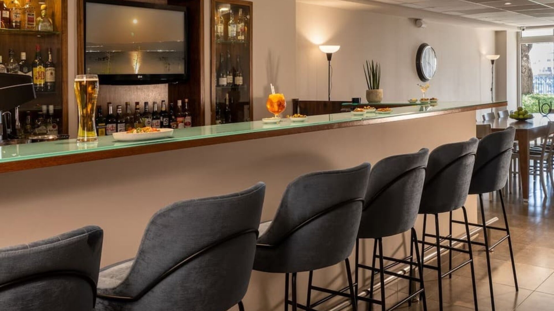 Hotel bar with a long counter, grey upholstered stools and a display of drinks at Prima Galil Tiberias.