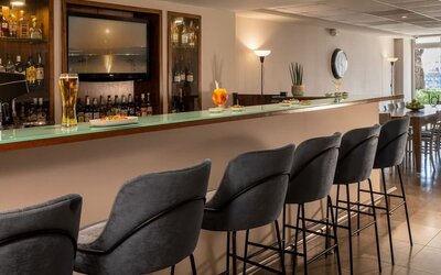 Hotel bar with a long counter, grey upholstered stools and a display of drinks at Prima Galil Tiberias.