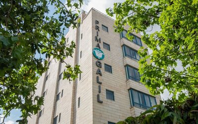 Exterior view of the hotel building surrounded by mature green trees at Prima Galil Tiberias.