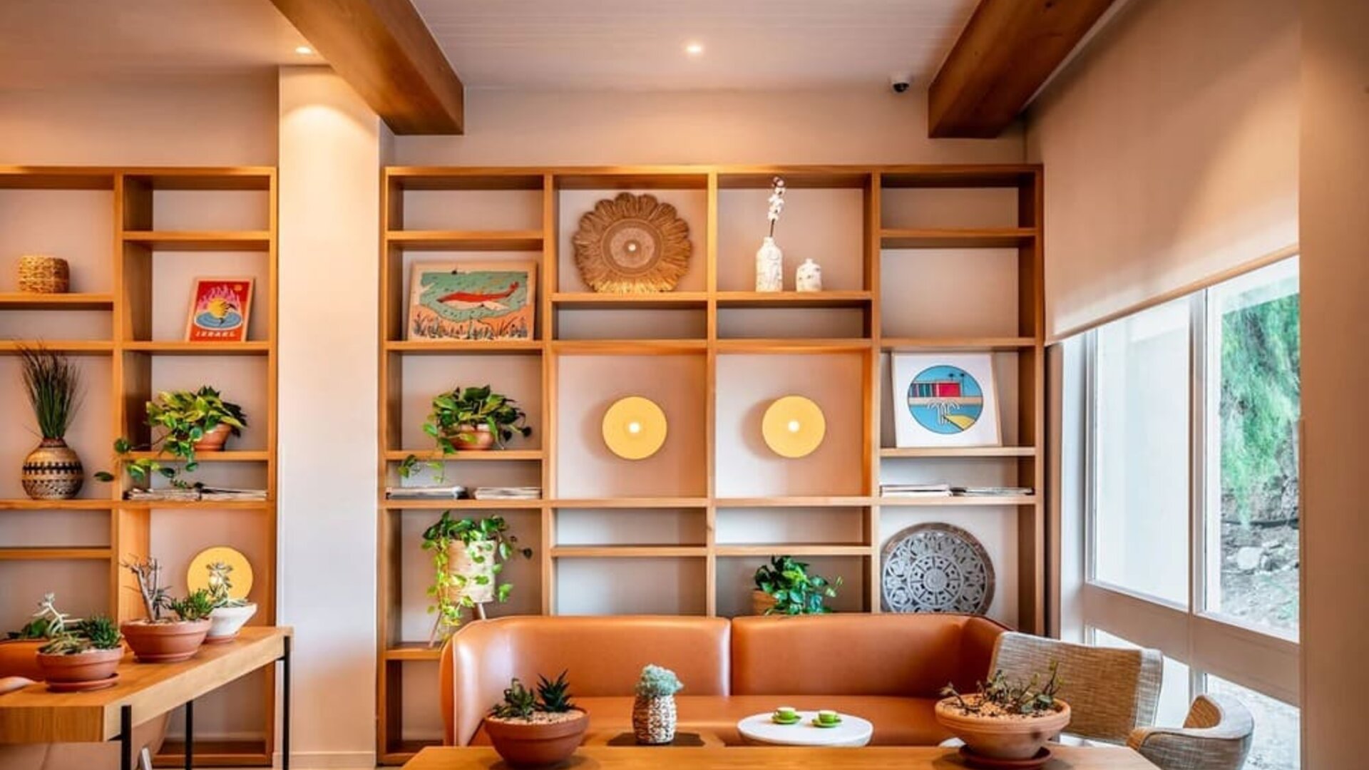 Lounge seating area with an orange sofa, wooden shelving, decorative objects and indoor plants at Prima Music Eilat.