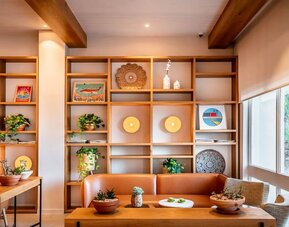 Lounge seating area with an orange sofa, wooden shelving, decorative objects and indoor plants at Prima Music Eilat.