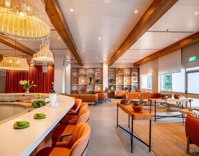 Restaurant and lounge area with orange bar stools, woven pendant lights, wooden ceiling beams and contemporary seating at Prima Music Eilat.