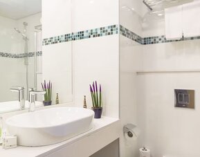 Bathroom with a white vessel sink, large mirror, chrome fixtures and blue-and-green mosaic tile accents at Prima Music Eilat.