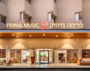 Exterior entrance to Prima Music Eilat, featuring illuminated hotel signage and glass entrance doors.