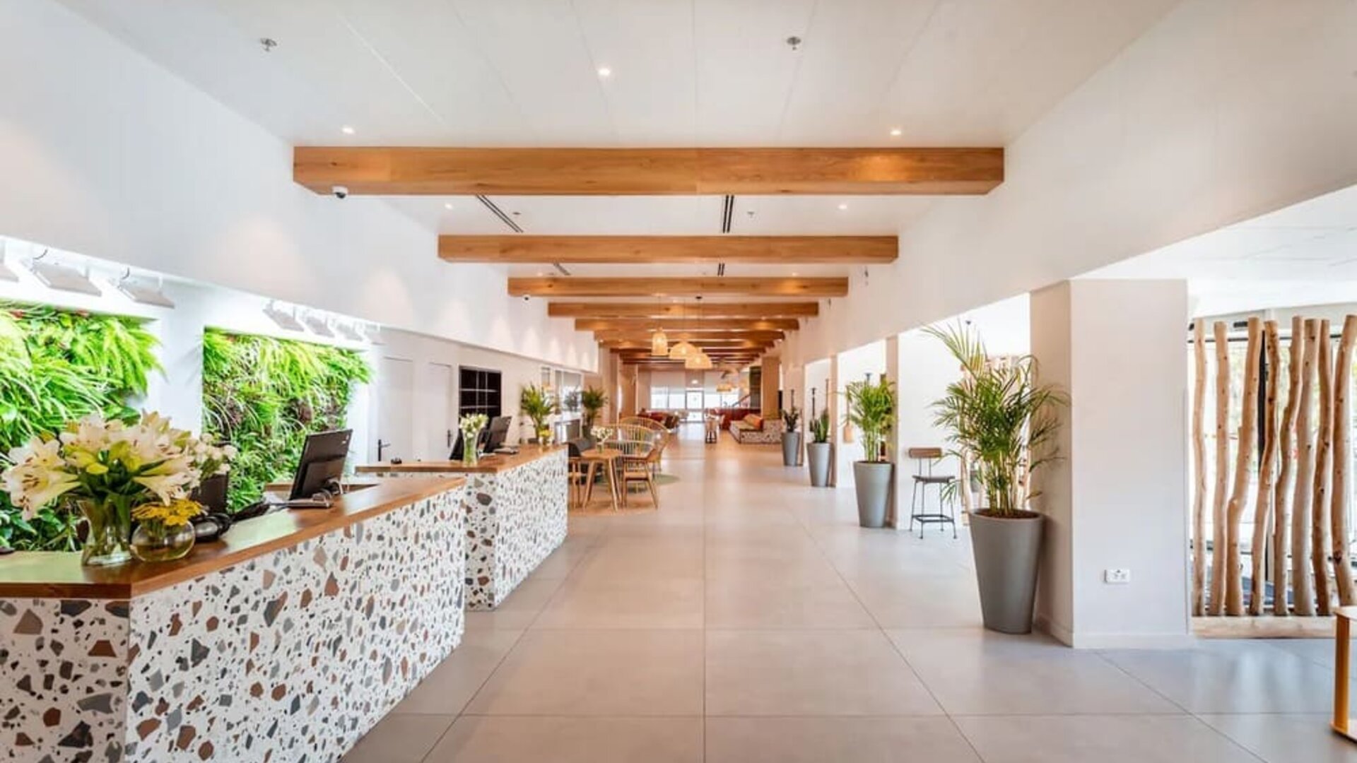 Hotel reception area with a decorative stone-fronted desk, greenery and a long, bright lobby at Prima Music Eilat.