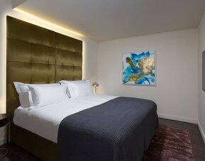 Guest room with king bed, gold upholstered headboard, bedside tables and wall-mounted television at Lady Stern Hotel.