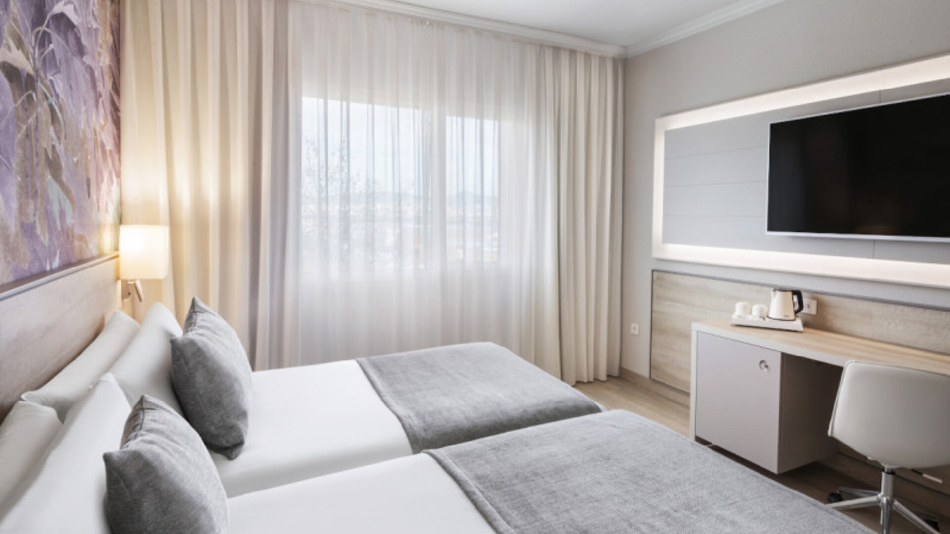 Twin bedroom with two single beds, grey runners, a desk, wall-mounted television and large curtained window at Hotel Sallés Ciutat del Prat.
