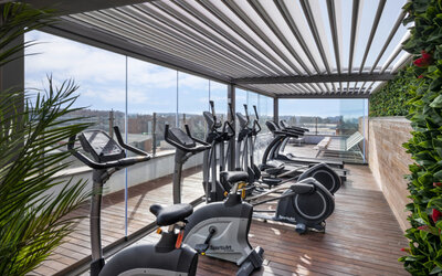 Rooftop fitness centre equipped with stationary bikes, treadmills and exercise machines beside glass railings at Hotel Sallés Ciutat del Prat.