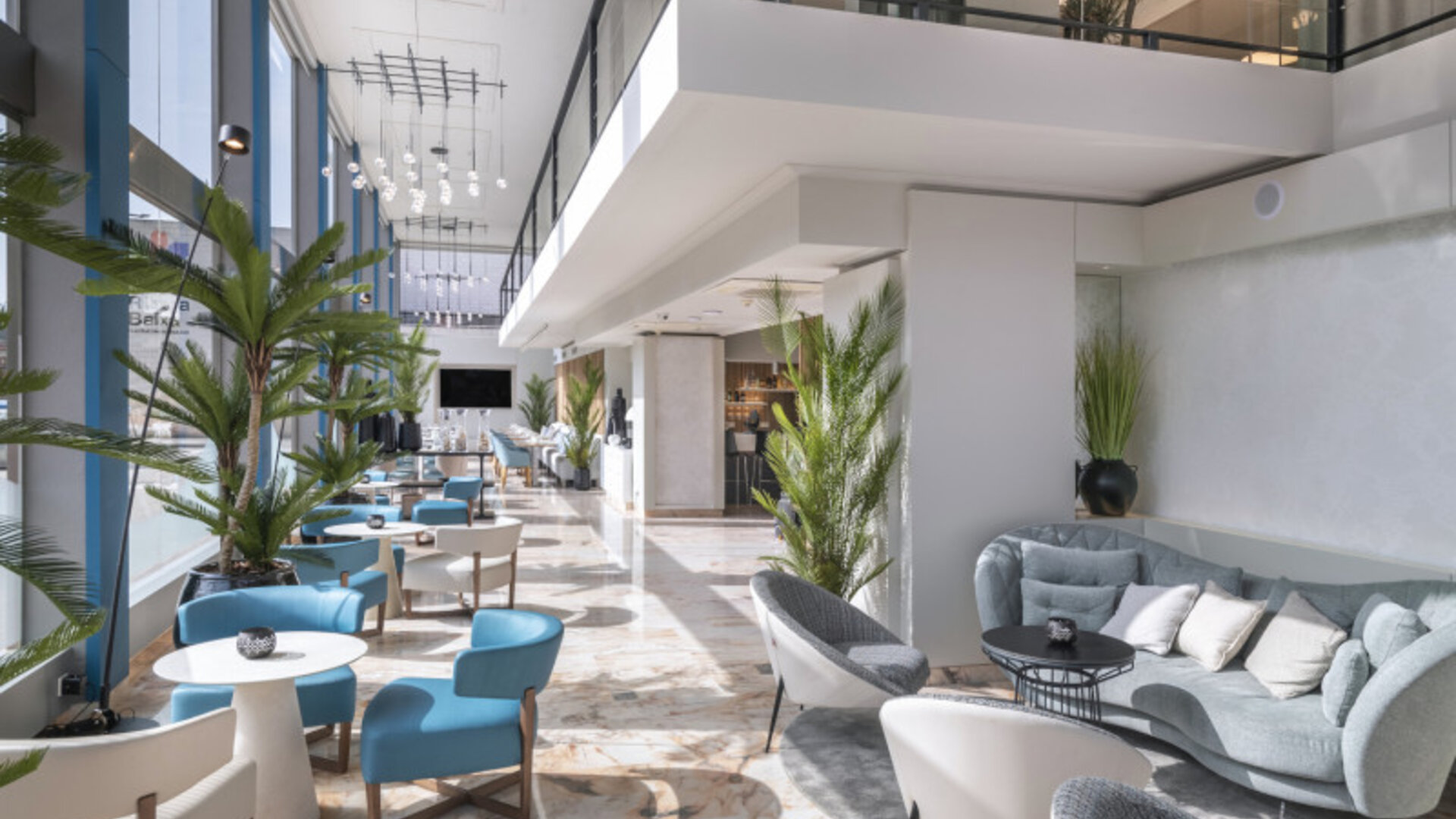 Spacious hotel lobby with grey sofas, modern armchairs, indoor plants and polished marble flooring at Hotel Sallés Ciutat del Prat.