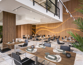 Restaurant seating with round tables, dark chairs and a circular vertical garden mounted on the wall at Hotel Sallés Ciutat del Prat.