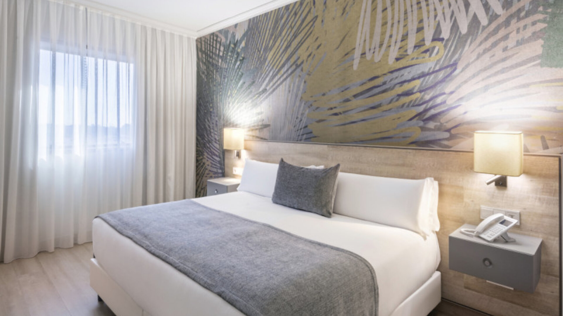 Guest bedroom with a king-size bed, grey bedding, white curtains and a colourful abstract feature wall at Hotel Sallés Ciutat del Prat.