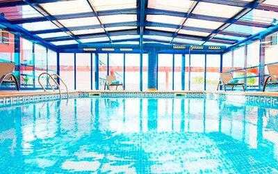 Indoor swimming pool beneath a glass roof, surrounded by tiled flooring and large windows at Hotel Sallés Ciutat del Prat.